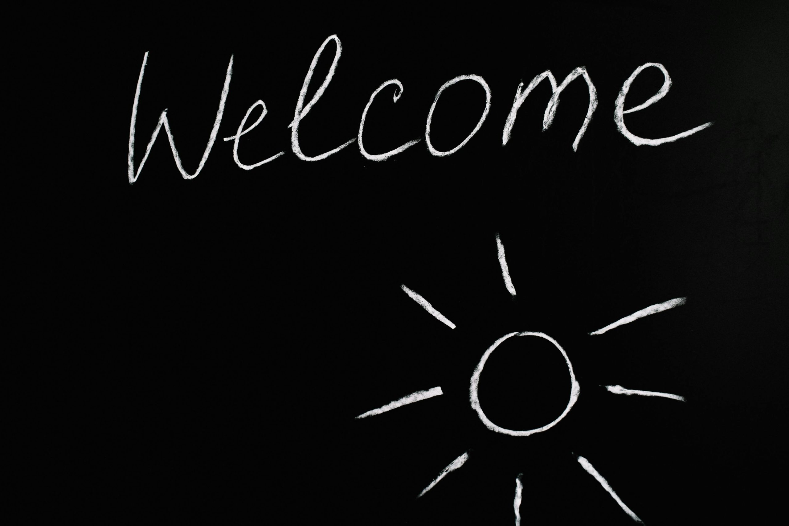 Chalk-drawn 'Welcome' and sun illustration on a black chalkboard background.